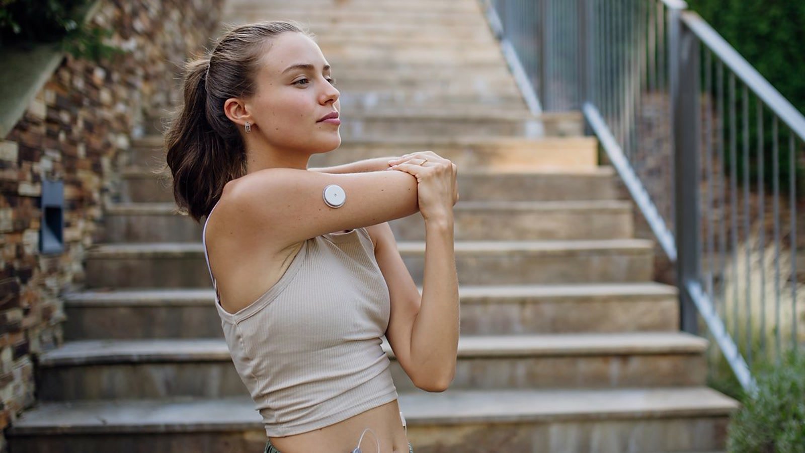 A woman stretching outdoors with a LinX sensor visible on her upper arm